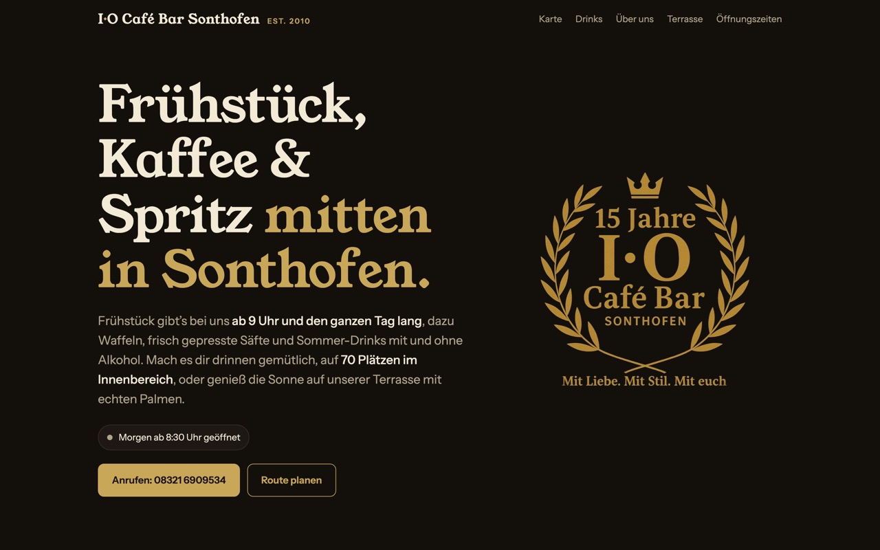 Startseite der I·O Café Bar Sonthofen: dunkles Design mit goldener Schrift und dem Jubiläums-Logo